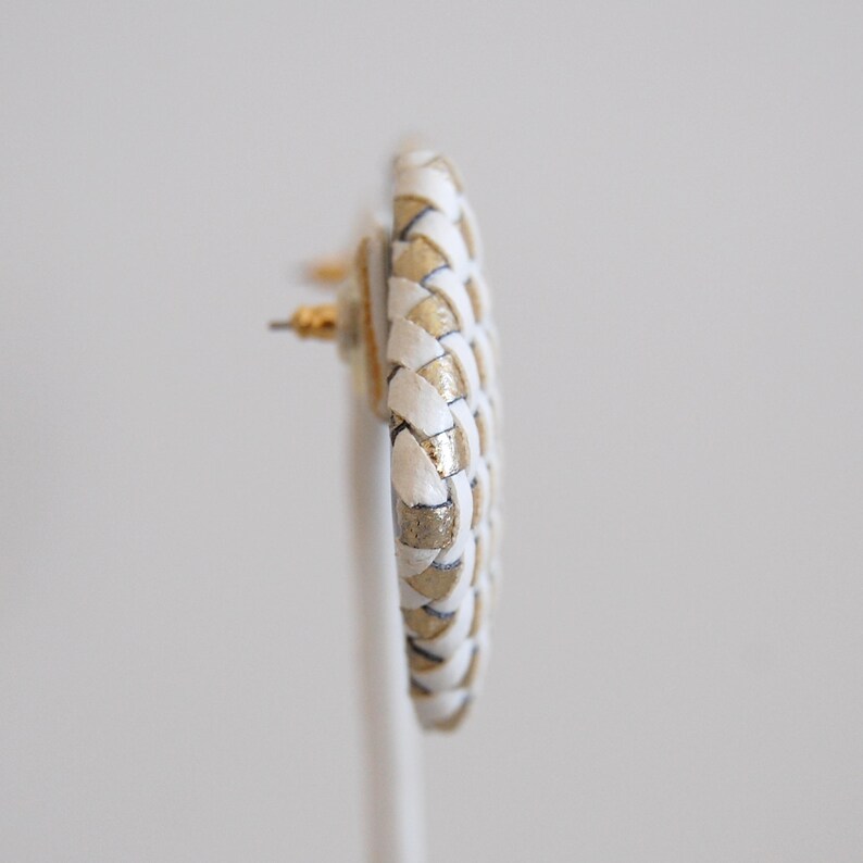 Op de afbeelding: Een paar witte en gouden geweven creolen. De oorbellen zijn gemaakt van een gevlochten materiaal met een gouden accent.