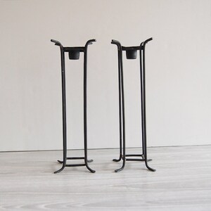Puede incluir: Un par de candelabros de metal negro con un dise&ntilde;o geom&eacute;trico simple. Cada candelabro tiene una base cuadrada y un marco rectangular.