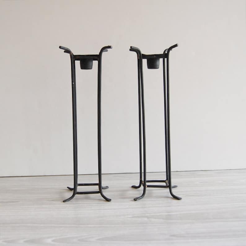 Puede incluir: Un par de candelabros de metal negro con un dise&ntilde;o geom&eacute;trico simple. Cada candelabro tiene una base cuadrada y un marco rectangular.