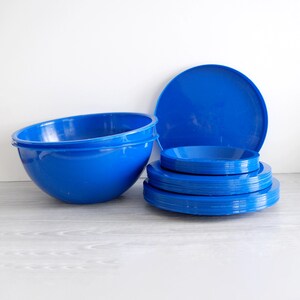 Może przedstawiać: Zestaw jasnoniebieskich plastikowych naczyń, w tym duża miska, stos talerzy i duży p&oacute;łmisek. Przedmioty są ułożone na jasnoszarej powierzchni na białym tle. Naczynia są w tym samym odcieniu niebieskiego.