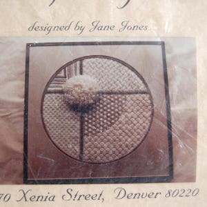 May include: A close-up of a beige and brown embroidery pattern with a circle design. The pattern is divided into four sections, each with a different stitch. The text "designed by Jane Jones" is visible at the top of the image. The text "70 Xenia Street, Denver 80220" is visible at the bottom of the image.