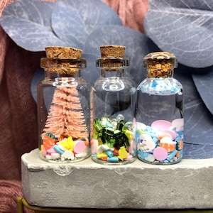 May include: Three small glass bottles with cork tops filled with colorful sprinkles and a miniature pink Christmas tree.