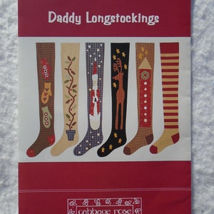 May include: A red and white paper with the text "Daddy Longstockings" and "cabbage rose" printed on it. The image shows six different Christmas stocking designs with various patterns and colors, including mittens, holly, and reindeer.