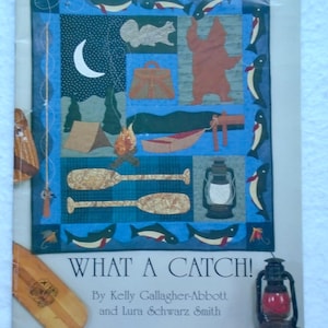 May include: A quilt pattern titled "WHAT A CATCH!" features a camping theme with a crescent moon, bear, fish, and paddles. The design includes a tent, campfire, and a lantern. The pattern is by Kelly Gallagher-Abbott and Lura Schwarz Smith.