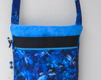 May include: A blue crossbody bag with a dragonfly pattern. The bag features a blue strap, a blue top, a black stripe, and a zippered pocket. The dragonfly pattern is in shades of blue and white.