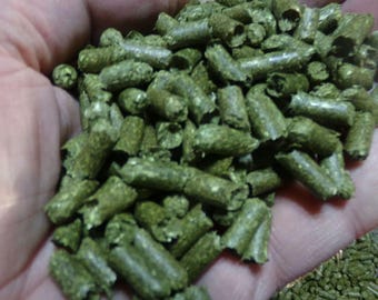 Può includere: Primo piano di una manciata di pellet cilindrici verdi. I pellet sono di un colore verde tenue e sembrano essere compressi. L'immagine è ben illuminata, mostrando la consistenza e la forma dei pellet.