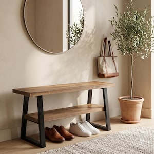 Può includere: Una panca in legno con un ripiano inferiore e gambe in metallo nero. Due paia di scarpe sono posizionate sotto la panca. Uno specchio rotondo è appeso al muro sopra la panca. Una borsa tote è appesa al muro a destra dello specchio. Una pianta in vaso è a destra della borsa.