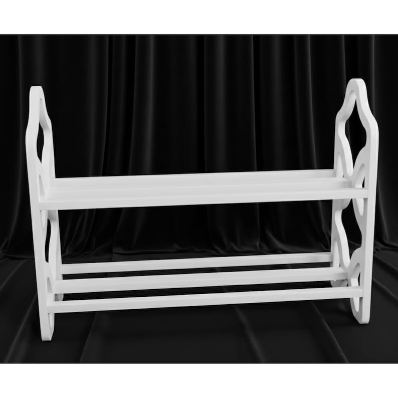 May include: A white wooden shoe rack with two shelves and decorative side supports. The rack has a simple, clean design, perfect for organizing footwear. The rack is made of wood and is painted white.