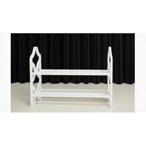 May include: A white wooden shoe rack with two shelves. The rack has decorative cutouts on the sides and is designed to hold multiple pairs of shoes. The background is a black curtain.
