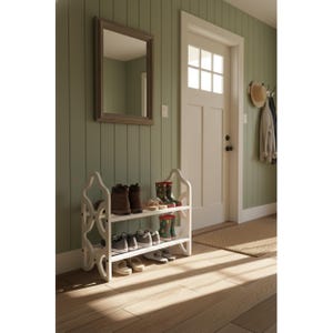 May include: A white, two-tiered shoe rack with an ornate design, holding various shoes and boots. The rack is positioned in a hallway with a green wall, a mirror, and a white door. The floor is made of wood.