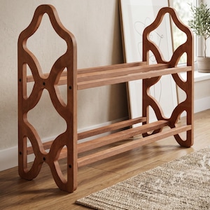 May include: A wooden shoe rack with a decorative, openwork design. The rack has three shelves and is made of light brown wood. The sides feature an intricate, geometric pattern. The shoe rack is placed on a wooden floor.