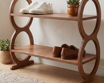 May include: A two-tiered wooden shoe rack with a unique, open-circle design on the sides. The top shelf holds white sneakers, while the bottom shelf displays brown leather loafers. A small potted succulent sits on the top shelf. The rack is made of light brown wood.