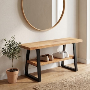 Peut inclure: Banc en bois avec une étagère inférieure, soutenu par des pieds en métal noir. Le banc a une finition en bois naturel et mesure environ 122 cm de long. Des chaussures sont placées sur l'étagère. Un miroir rond est accroché au mur au-dessus du banc.