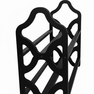 May include: Black wooden wine rack with a decorative, openwork design. The rack has a curved top and holds multiple bottles. The design features geometric cutouts and horizontal supports, suitable for home decor.