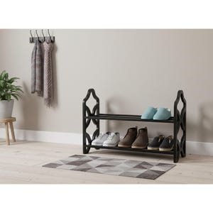 May include: A black two-tier shoe rack with a decorative design on the sides. The rack holds various shoes, including sneakers, boots, and slippers. A patterned rug sits beneath the rack. Scarves hang on a wall hook above the rack.