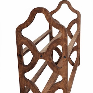 May include: A wooden wine rack with a dark brown finish. The rack has a decorative, openwork design with curved edges and holds multiple bottles. The construction features horizontal supports and is held together with black hardware.