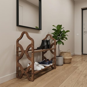 May include: A two-tier wooden shoe rack with a dark brown finish and curved, decorative side panels. The rack holds a pair of black ankle boots on the top shelf and two pairs of low-top trainers, one white and one navy blue, on the bottom shelf.