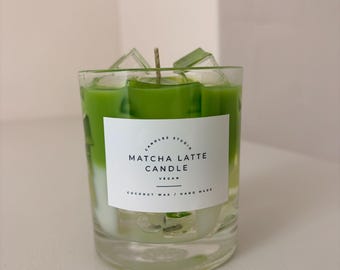 May include: A clear glass candle filled with green matcha latte coloured wax and translucent ice cube shapes. A white rectangular label on the front reads CANDLES STUDIO MATCHA LATTE CANDLE VEGAN COCONUT WAX / HAND MADE with a single central wick.