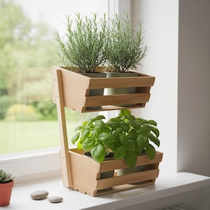 Może przedstawiać: Dwupoziomowa drewniana donica z roślinami rozmarynu i bazylii w zielonych doniczkach. Donica wykonana jest z jasnego drewna i stoi na białym parapecie. Tło przedstawia rozmyty widok zielonej przestrzeni na zewnątrz.