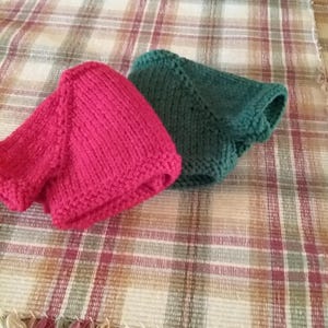May include: Two knitted hats, one red and one green, are displayed on a plaid fabric background.