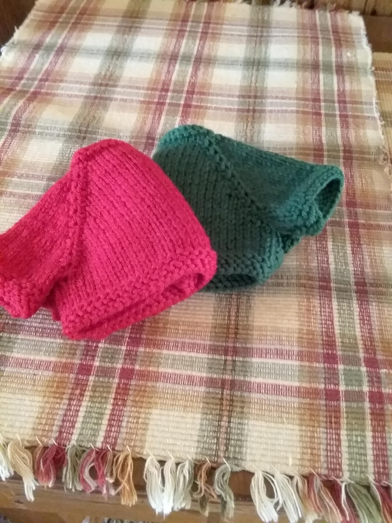 May include: Two knitted hats, one red and one green, are displayed on a plaid fabric background.