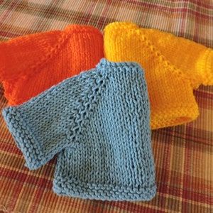 May include: Three knitted sweaters in different colors: orange, blue, and yellow. The sweaters are folded and stacked on top of each other.