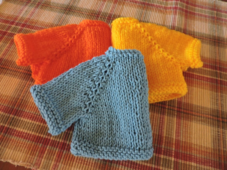 May include: Three knitted sweaters in different colors: orange, blue, and yellow. The sweaters are folded and stacked on top of each other.