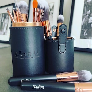 Puede incluir: Un conjunto de pinceles de maquillaje negros y oro rosa en dos estuches de cuero negro. Los estuches tienen el texto "adorn u" y "specialized makeup brushes". Los pinceles están etiquetados como "N-line" y "Nadine".
