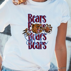 Può includere: Una maglietta bianca con un'immagine di un orso marrone e il testo "Bears  Bears  Bears" in lettere rosse e blu.