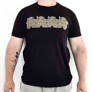 Op de afbeelding: Zwart T-shirt met een afbeelding van vijf bruine figuren in een rij, elk met een geweer op hun schouder.