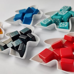 Può includere: Cinque piatti in ceramica bianca a forma di persone, ognuno con dadi di colori diversi. I dadi sono blu, turchese, neri, rossi e arancioni.