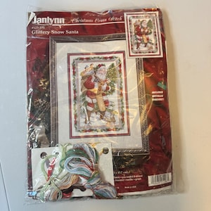 May include: A Janlynn Christmas Cross Stitch kit titled Glittery Snow Santa, #125-196. The package features a Santa illustration, metallic threads, and a 12 inch by 18 inch finished size. Includes fabric, pre-sorted 6-strand floss, needle, and graph.