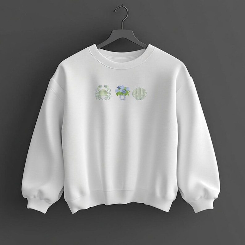 May include: White sweatshirt with embroidered designs of a crab, blue flowers, and a seashell. The sweatshirt has a crew neck and long sleeves. The embroidered designs are in shades of green and blue.
