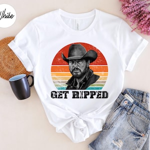 Może przedstawiać: Biała koszulka z grafiką w stylu vintage przedstawiającą mężczyznę w kowbojskim kapeluszu i napisem "GET RIPPED".