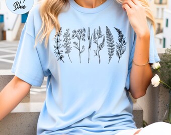 May include: A light blue t-shirt featuring a graphic of seven different types of black and white botanical illustrations.