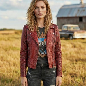 Peut inclure: Veste rouge à effet peau de serpent, de style motard classique, avec un col cranté et une fermeture éclair asymétrique. Portée sur un t-shirt graphique gris foncé et un jean noir délavé. Le t-shirt présente un graphisme de groupe.