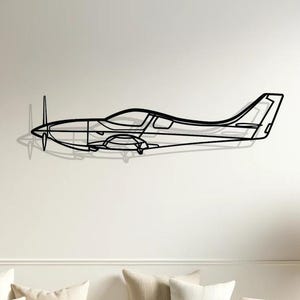 Può includere: Scultura da parete in metallo nero di un piccolo aereo. La scultura è montata su una parete bianca sopra un divano bianco con cuscini beige.