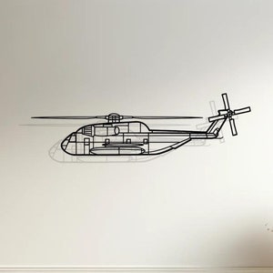 May include: A black metal wall art sculpture of a helicopter in a minimalist style. The helicopter is suspended against a white wall, above a white sofa with beige cushions. The sofa is in a living room setting with a wooden floor and a side table with a vase of dried flowers.