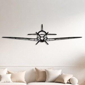 May include: A black metal airplane wall art piece. The artwork is mounted on a white wall above a light-colored sofa with beige pillows. The airplane has detailed wings and a propeller.