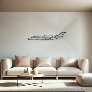 May include: A black metal outline of a private jet hangs on a white wall above a beige sectional sofa with three cushions. The sofa is in a living room with a wooden coffee table and a beige ottoman.