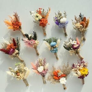 May include: A collection of small, dried flower bouquets. Each bouquet features a variety of colors, including orange, white, purple, and yellow. The stems are wrapped with twine. These bouquets are ideal for home decor or special events.