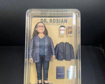 以下が含まれることがあります： 透明なケースに入った、心理学者であるDr. Rosianのフィギュア。フィギュアはメガネ、青いジャケット、黒いズボンを着用しています。付属品には、ミニチュアジャケット、コーヒーカップ、Unoカード、DSM-5-TRの本が含まれています。