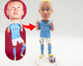Può includere: Una statuetta personalizzata con la testa oscillante di un calciatore che indossa una maglia blu chiaro con la scritta "Etihad Airways" sul davanti. La statuetta tiene le braccia alzate in aria con i pollici rivolti verso l'alto. La statuetta è in piedi su una base bianca con un pallone da calcio ai suoi piedi.