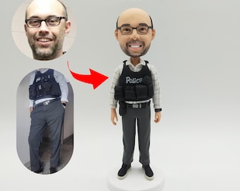 May include: A custom-made figurine of a person wearing a black and white checkered shirt, black vest with the word "Police" on it, and gray pants. The figurine is standing on a white base.
