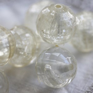 May include: A close-up of a string of clear, faceted glass beads. The beads are round and have a slightly iridescent sheen.