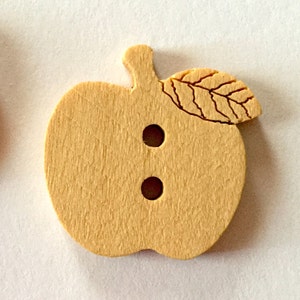 May include: A wooden apple-shaped button with a leaf detail and two holes for sewing. The button is light brown in color.