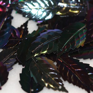 May include: A pile of iridescent black leaf-shaped sequins. The sequins have a metallic sheen and are perfect for crafting and decorating.