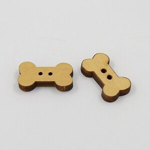 May include: Two wooden bone-shaped buttons with two holes each. The buttons are light brown and have a smooth finish.