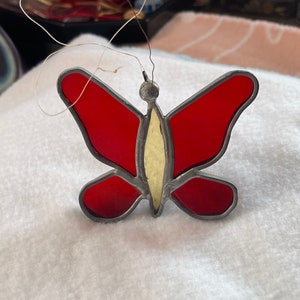 May include: A red stained glass butterfly ornament with a white center. The butterfly is hanging from a string.