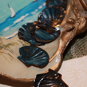 May include: A decorative seashell dish with a gold finish and blue and black seashell accents. The dish is made of ceramic and has a textured surface.